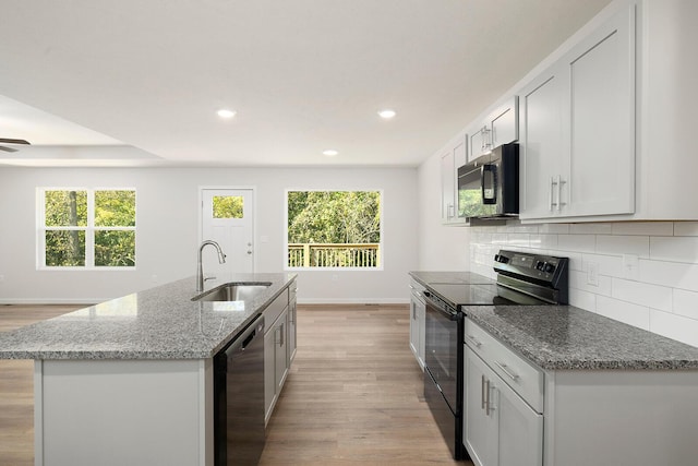 kitchen featuring sink, white cabinetry, light stone counters, black appliances, and an island with sink