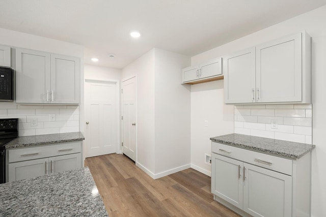 kitchen with tasteful backsplash, black appliances, light hardwood / wood-style flooring, and stone counters