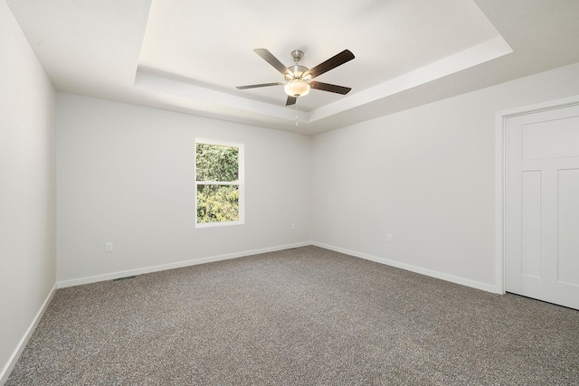 empty room with a tray ceiling, ceiling fan, and carpet flooring