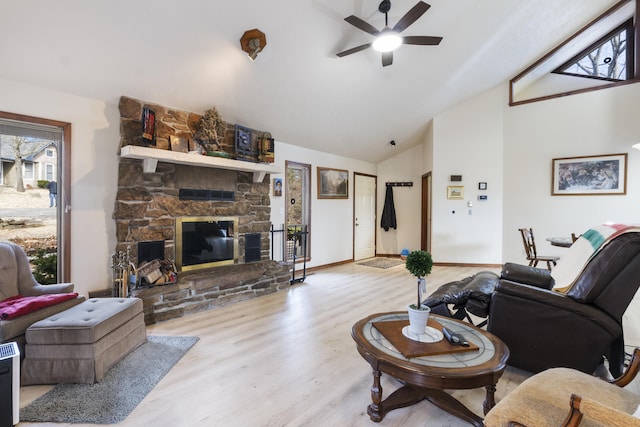 living room with lofted ceiling, a stone fireplace, ceiling fan, and light wood-type flooring