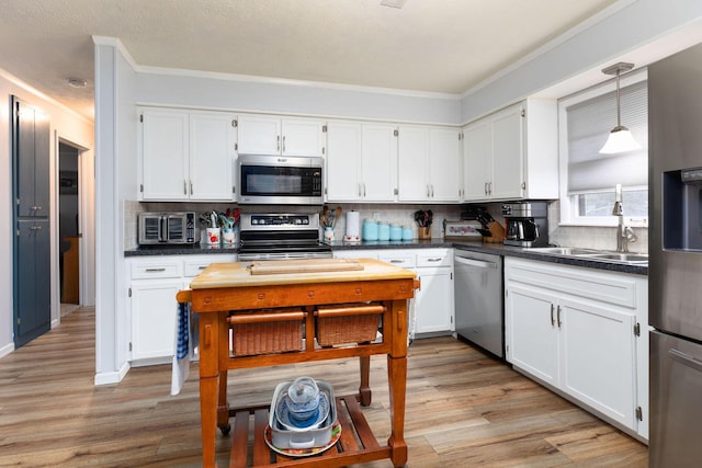 kitchen with stainless steel appliances, white cabinets, and decorative light fixtures