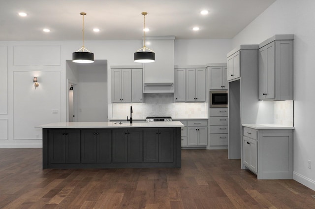 kitchen with pendant lighting, gray cabinetry, a kitchen island with sink, built in microwave, and decorative backsplash