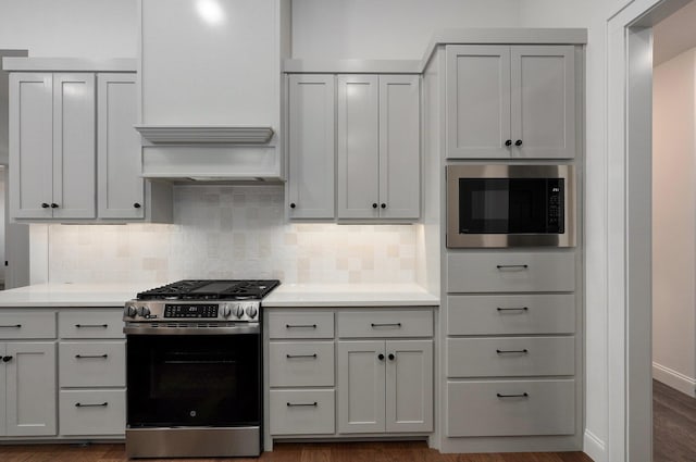 kitchen featuring gray cabinetry, stainless steel appliances, tasteful backsplash, dark hardwood / wood-style flooring, and custom exhaust hood