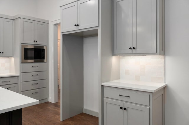 kitchen featuring gray cabinets, tasteful backsplash, dark wood-type flooring, and stainless steel microwave