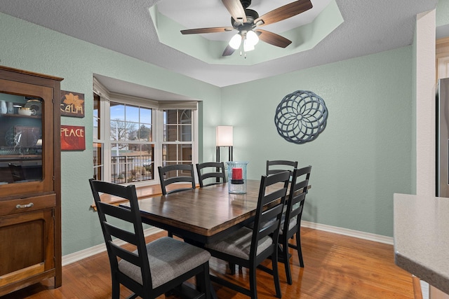 dining area featuring hardwood / wood-style flooring, ceiling fan, and a raised ceiling