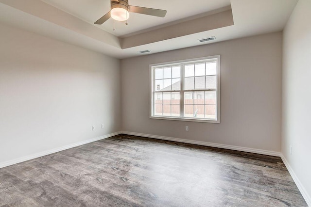 unfurnished room with a raised ceiling, hardwood / wood-style floors, and ceiling fan