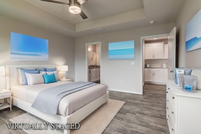 bedroom featuring ceiling fan, ensuite bathroom, dark hardwood / wood-style floors, and a raised ceiling