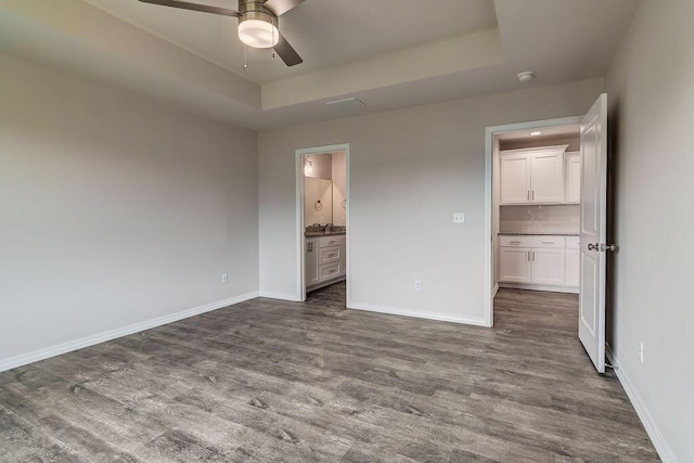 unfurnished bedroom featuring dark hardwood / wood-style flooring, connected bathroom, a tray ceiling, and a spacious closet