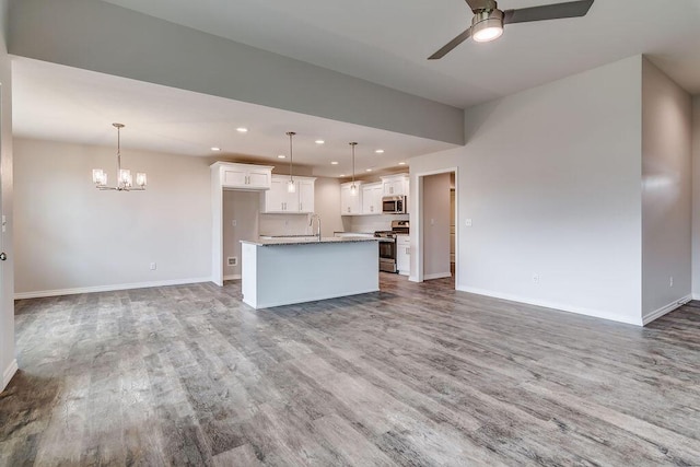 kitchen with decorative light fixtures, appliances with stainless steel finishes, a kitchen island with sink, ceiling fan with notable chandelier, and white cabinets