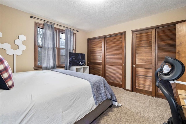 bedroom with a textured ceiling, multiple closets, and carpet flooring