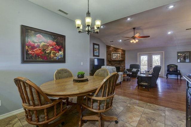 dining space with lofted ceiling, ceiling fan with notable chandelier, a stone fireplace, and french doors