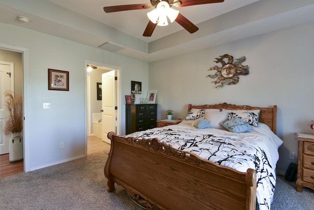 carpeted bedroom with a raised ceiling, ensuite bathroom, and ceiling fan