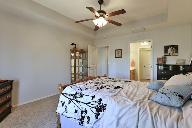 carpeted bedroom featuring a tray ceiling, ensuite bath, and ceiling fan