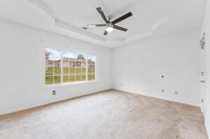 unfurnished room with a raised ceiling, ceiling fan, and carpet