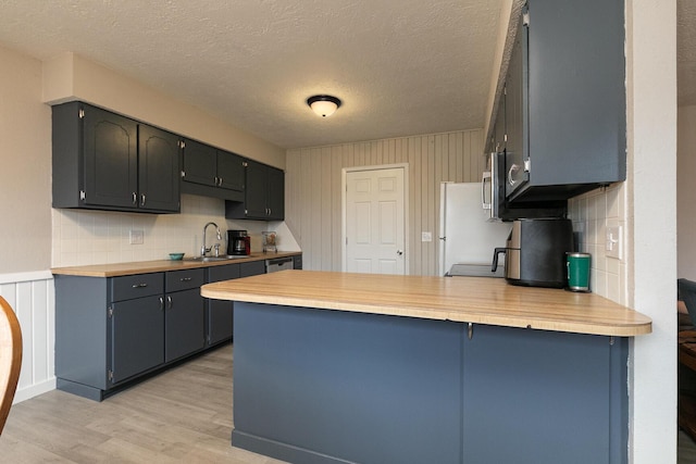 kitchen with sink, fridge, kitchen peninsula, light hardwood / wood-style floors, and backsplash