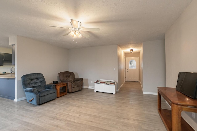 living area with ceiling fan, light hardwood / wood-style floors, and a textured ceiling