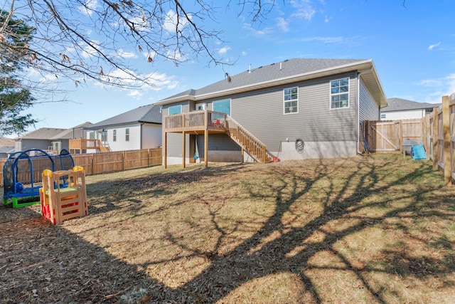 back of property with a wooden deck, a yard, a playground, and a trampoline