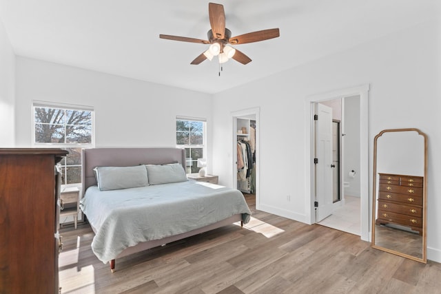 bedroom featuring light wood-type flooring, a walk in closet, ceiling fan, ensuite bath, and a closet