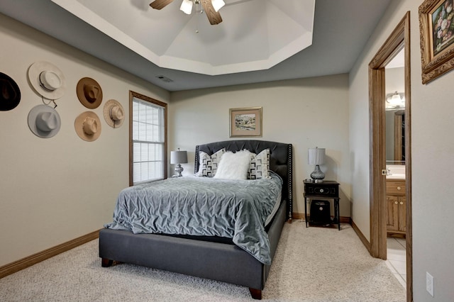 carpeted bedroom featuring a tray ceiling, ensuite bath, and ceiling fan