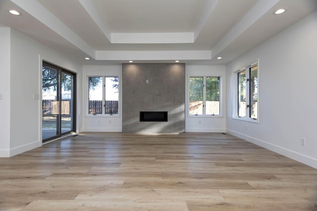 unfurnished living room featuring a tile fireplace, light hardwood / wood-style floors, and a tray ceiling