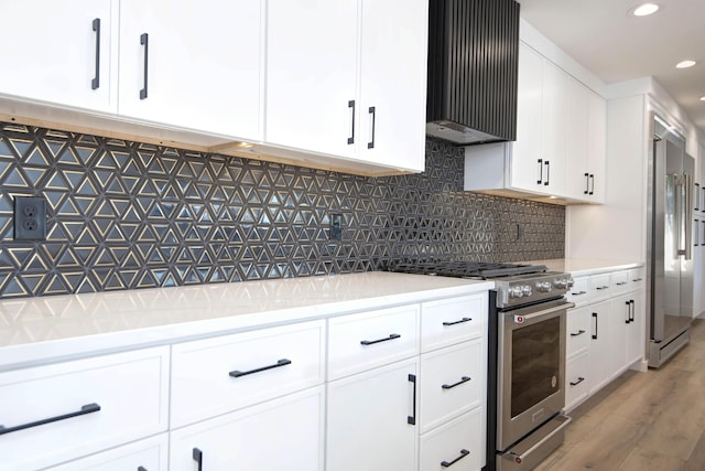 kitchen with wall chimney exhaust hood, light hardwood / wood-style flooring, premium appliances, white cabinets, and backsplash