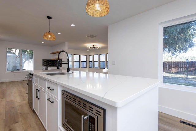 kitchen featuring stainless steel microwave, decorative light fixtures, sink, a kitchen island with sink, and light stone countertops