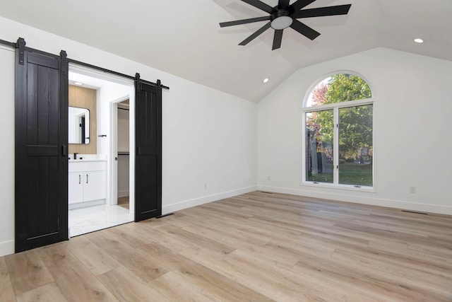 interior space featuring vaulted ceiling, a barn door, ceiling fan, and light hardwood / wood-style flooring