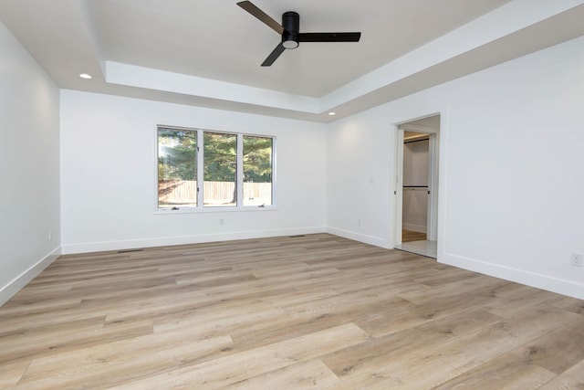 unfurnished room with light hardwood / wood-style flooring, a raised ceiling, and ceiling fan