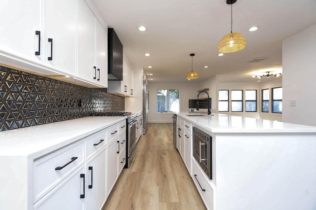 kitchen with sink, appliances with stainless steel finishes, an island with sink, pendant lighting, and white cabinets