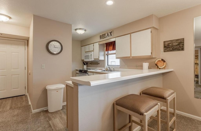 kitchen featuring electric range oven, kitchen peninsula, white cabinets, and a kitchen bar