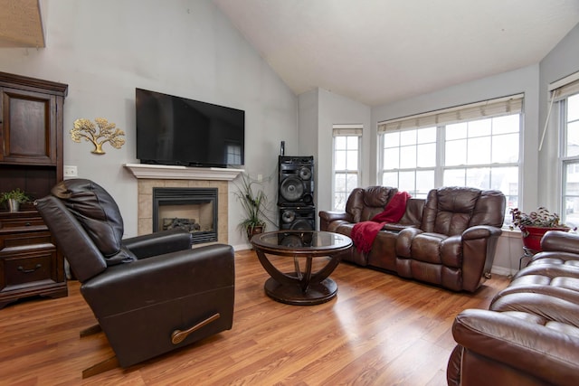 living room featuring high vaulted ceiling, a fireplace, and light hardwood / wood-style flooring