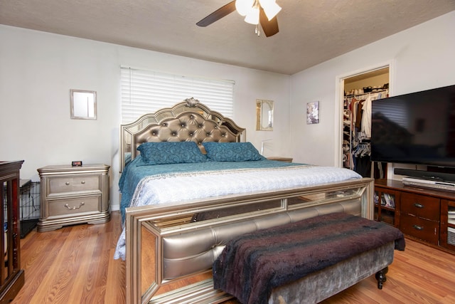 bedroom with ceiling fan, a spacious closet, a textured ceiling, and light wood-type flooring