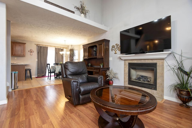 living room featuring a notable chandelier, a tile fireplace, a textured ceiling, and light wood-type flooring