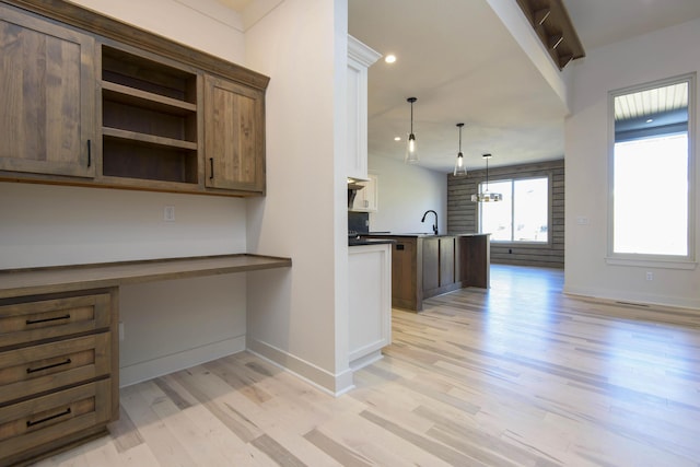 kitchen featuring built in desk, sink, hanging light fixtures, and light hardwood / wood-style flooring