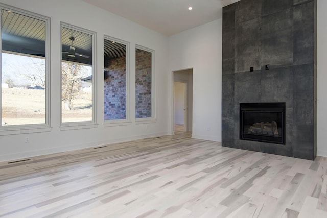 unfurnished living room with a high ceiling, a tile fireplace, and light hardwood / wood-style flooring