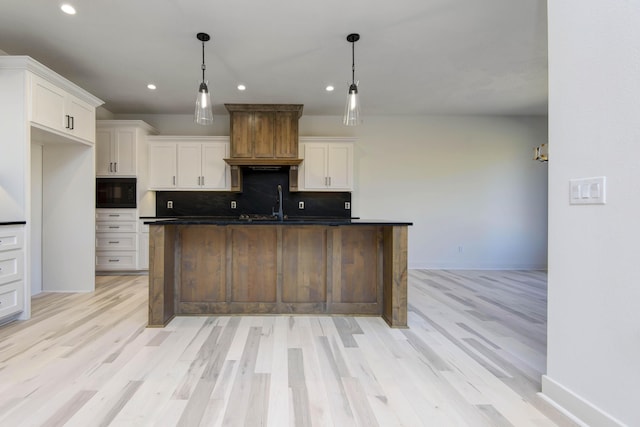 kitchen with black microwave, white cabinetry, a kitchen island with sink, and decorative light fixtures