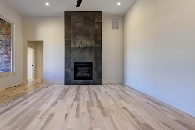 unfurnished living room with a tiled fireplace, light hardwood / wood-style flooring, and ceiling fan