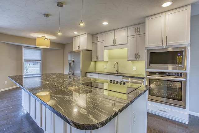 kitchen with white cabinetry, sink, dark stone countertops, hanging light fixtures, and stainless steel appliances