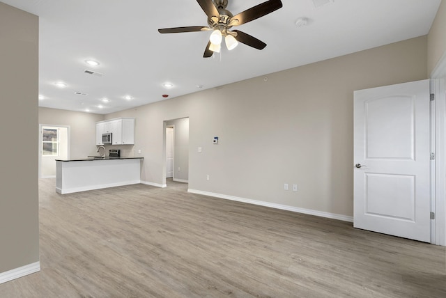 unfurnished living room featuring sink, ceiling fan, and light wood-type flooring