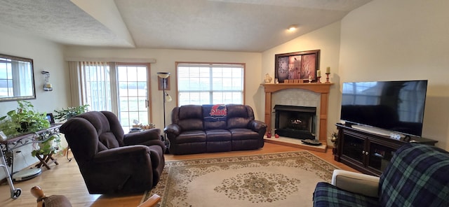 living room with a fireplace, vaulted ceiling, a textured ceiling, and light wood-type flooring