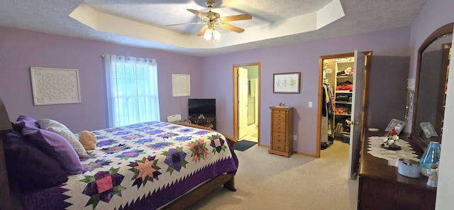 bedroom featuring a raised ceiling, a spacious closet, light carpet, and a textured ceiling