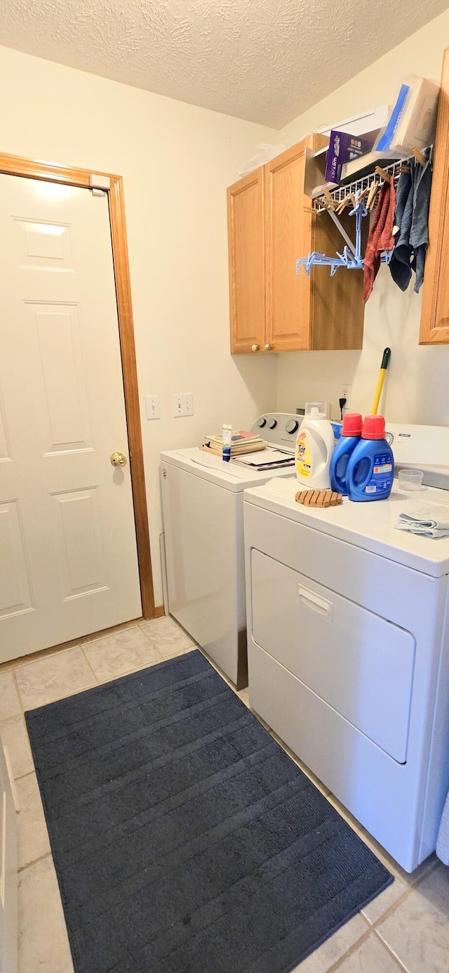 laundry area featuring cabinets, washer and clothes dryer, a textured ceiling, and light tile patterned floors