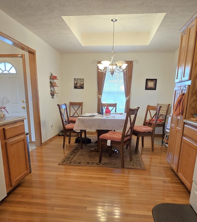 dining room featuring an inviting chandelier, a tray ceiling, light hardwood / wood-style flooring, and a textured ceiling