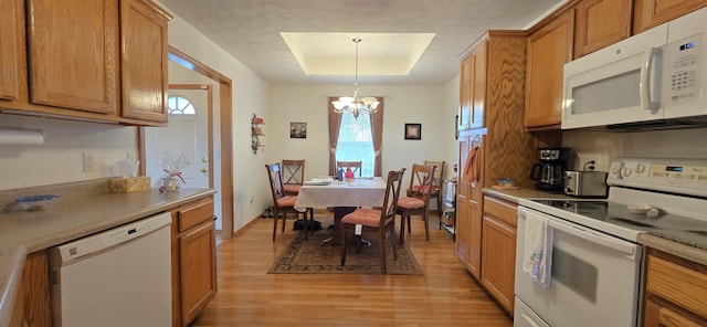 kitchen with pendant lighting, white appliances, an inviting chandelier, a tray ceiling, and light wood-type flooring