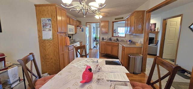 kitchen with sink, a chandelier, light wood-type flooring, pendant lighting, and white appliances