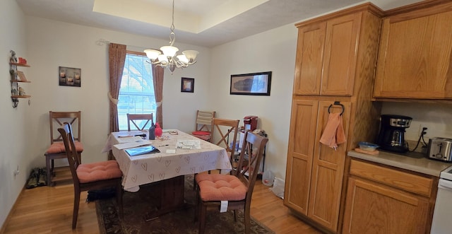 dining area featuring a chandelier, a raised ceiling, and light hardwood / wood-style flooring