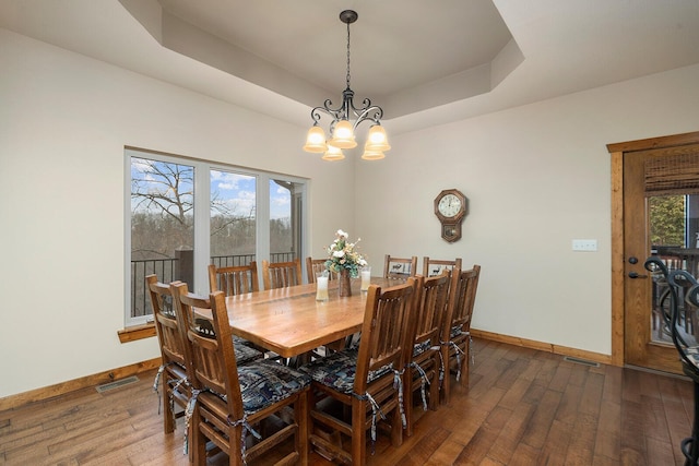 dining room with an inviting chandelier, a healthy amount of sunlight, dark hardwood / wood-style floors, and a raised ceiling