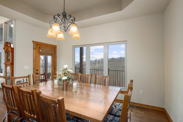 dining area with hardwood / wood-style floors, a tray ceiling, and a chandelier