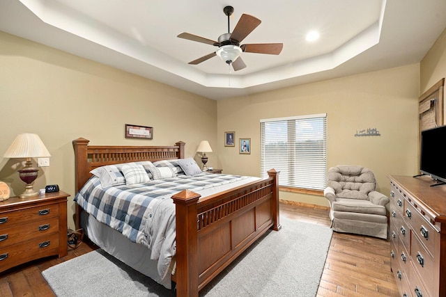 bedroom featuring ceiling fan, a raised ceiling, and light wood-type flooring