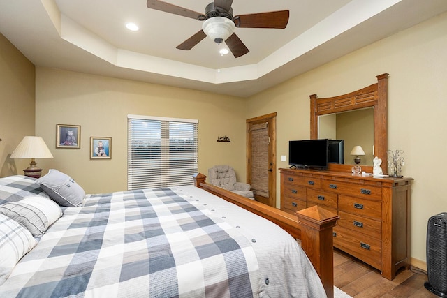 bedroom with ceiling fan, a raised ceiling, and light hardwood / wood-style floors